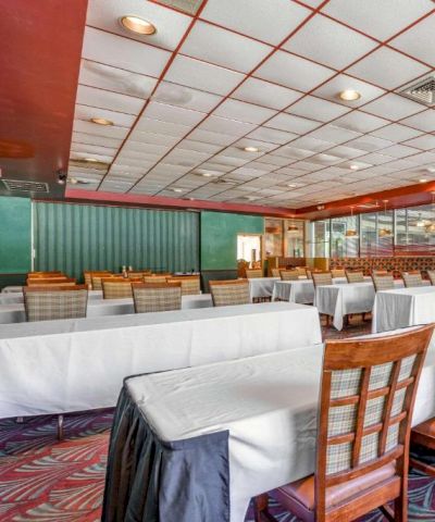 The image shows a spacious room with arranged tables and chairs, a projector screen, and patterned carpet, suitable for meetings or events.