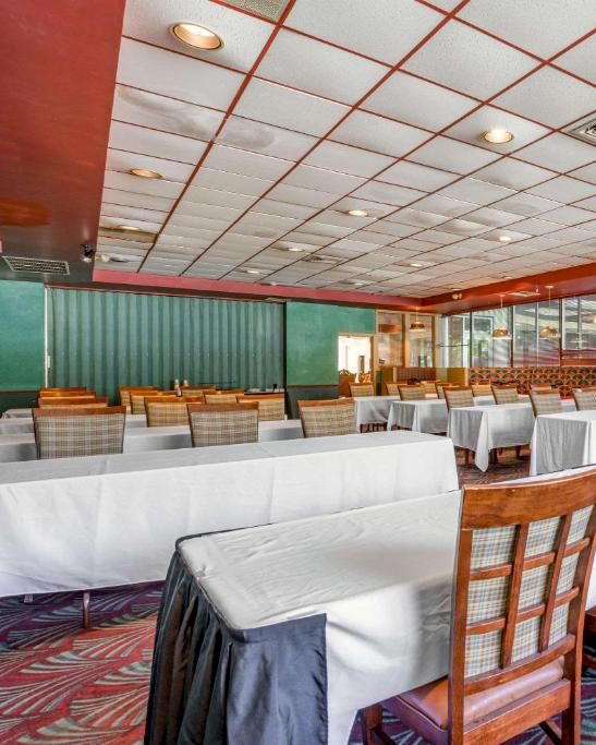 The image shows a spacious room with arranged tables and chairs, a projector screen, and patterned carpet, suitable for meetings or events.