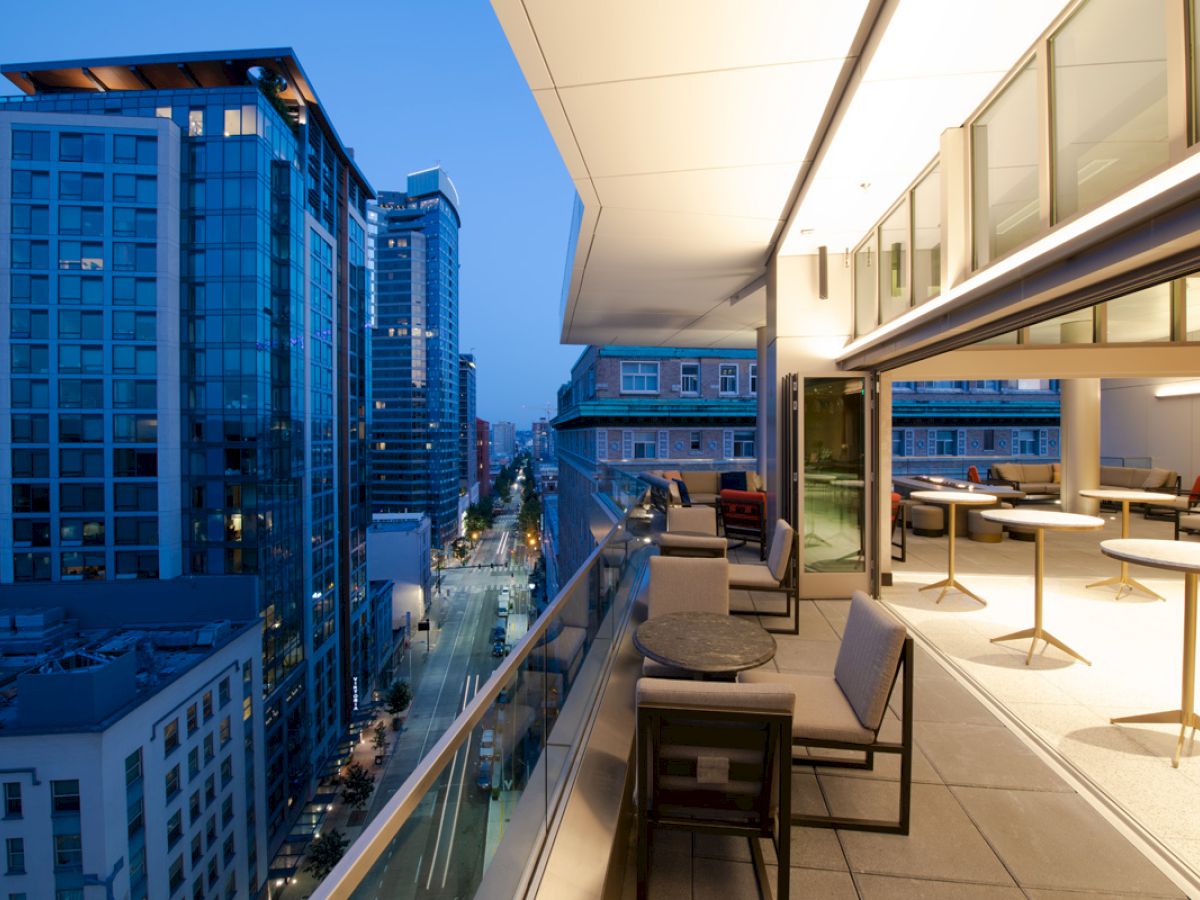 A modern rooftop patio with seating overlooks a cityscape of tall buildings at dusk, creating a serene urban atmosphere.