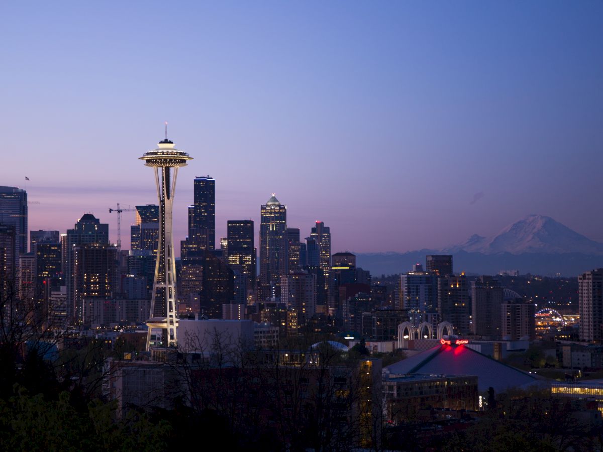 Seattle skyline at dusk featuring the Space Needle, with Mount Rainier visible in the background under a clear sky.