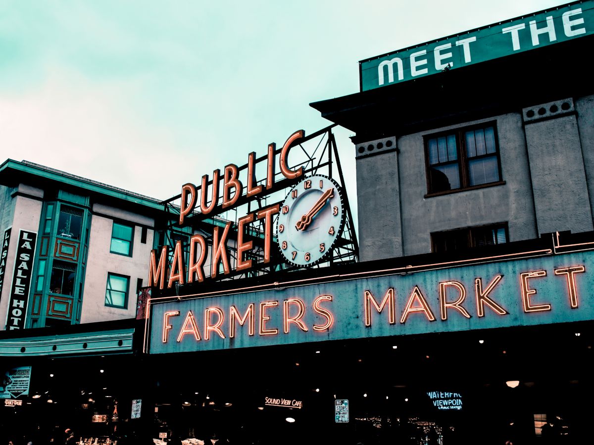 Neon signs for a "Public Market" and "Farmers Market" with a clock, buildings in the background, creating a vintage urban scene.